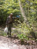 Paul (carrying bag of collected garbage) in bug jacket beside stand of red trilliums